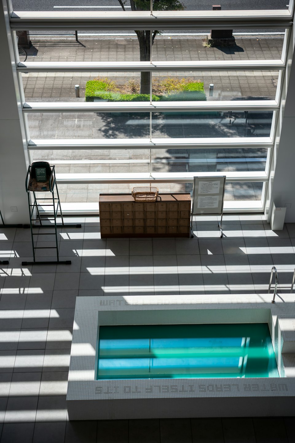 Empty indoor swimming pool with a lifeguard chair and wooden cabinet.